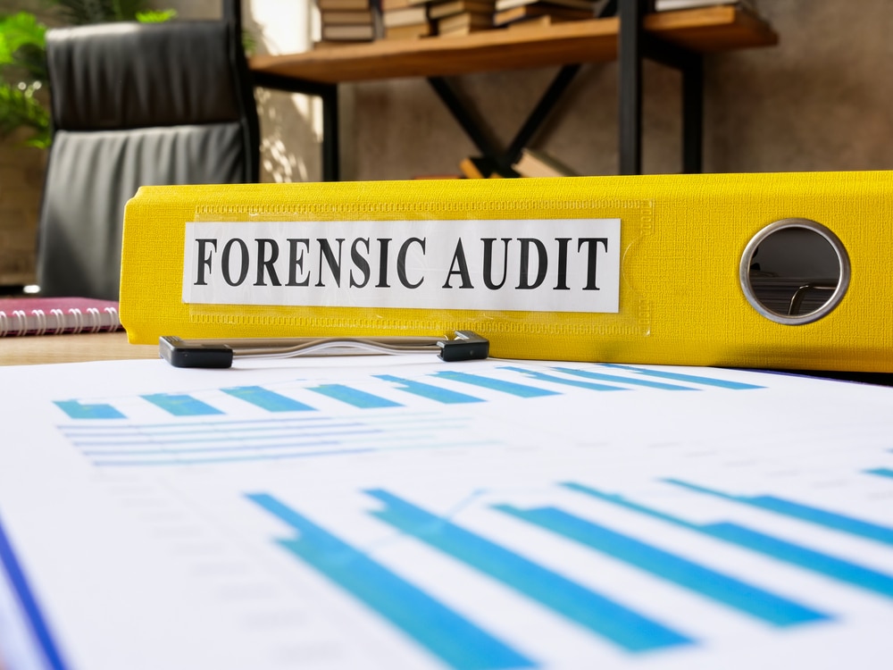 A binder labeled “forensic audit” sits on a desk.